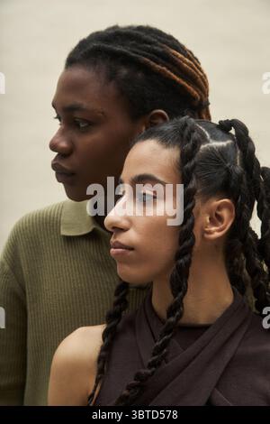 Jeune femme noire et jeune femme caucasienne debout ensemble face à face, toutes deux avec des cheveux tressés, montrant des expressions calmes, soulignant la diversité et l'amitié Banque D'Images