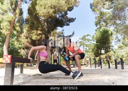 Entraîneur personnel motive une jeune femme effectuant des trempettes dans un parc de calisthenics en plein air, favorisant la forme physique et le bien-être Banque D'Images