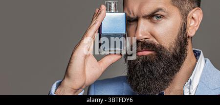 Beau jeune homme utilisant le parfum. Homme barbu pulvérisant du parfum de luxe, gros plan. Homme en costume formel, bouteille de parfum, gros plan Banque D'Images