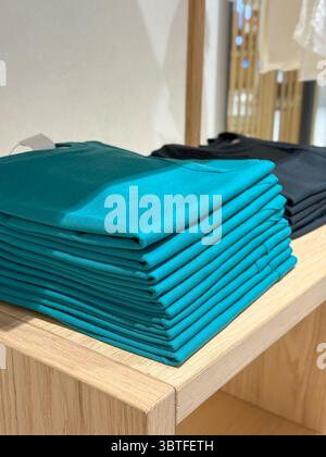 Chemises turquoise pliées sur l'étagère de vente au détail, pile soignée avec contraste de ton de terre Banque D'Images