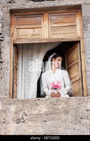 mariée regarde par une vieille fenêtre le jour de son mariage, paraissant heureuse. Journée des traditions chirches. Mariée des années 40 aux années 50 Banque D'Images
