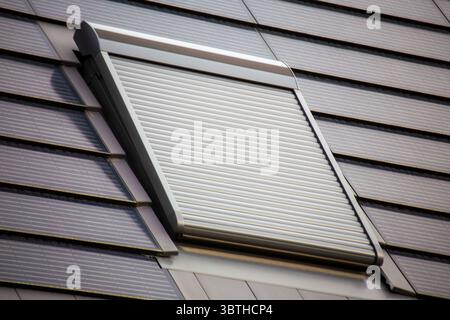 Fenêtre de toit avec volet roulant sur un toit recouvert de tuiles solaires Banque D'Images