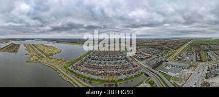Vue aérienne du complexe résidentiel semi-circulaire distinctif, bordé de canaux et de routes, s'étend vers l'horizon sous un ciel nuageux, Almere, Flevoland, pays-Bas. Banque D'Images