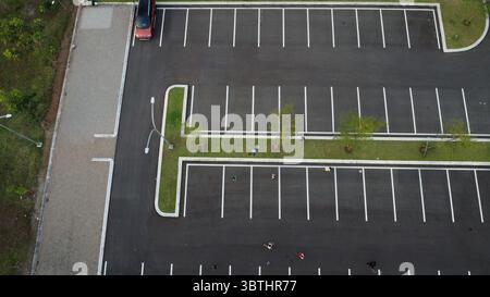 La vue aérienne présente un parking avec des espaces rayés, de la verdure et une voiture rouge solitaire, créant un paysage urbain. Banque D'Images