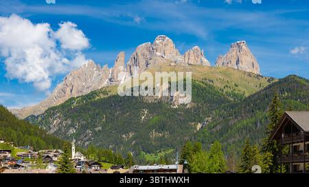 Les sommets majestueux de Cunturines s'élèvent au-dessus des vallées verdoyantes et du village alpin traditionnel de San Cassiano, Dolomites, sous un ciel clair. Banque D'Images