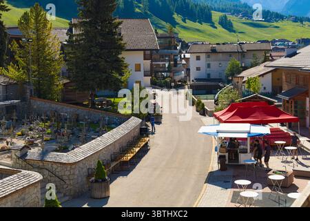 Une charmante scène de rue à San Cassiano, Dolomites, avec des bâtiments traditionnels, un stand de nourriture dynamique et un cimetière serein. Banque D'Images