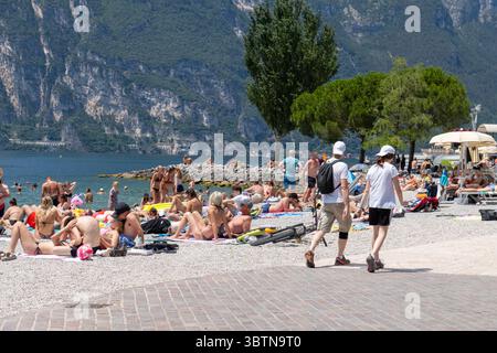 Nago-Torbole, Trentin, Italie - 15 juillet 2025 : les touristes apprécient la journée ensoleillée à Spiaggia Lungolago à Torbole sur la rive nord du lac de Garde. La plage de galets est très fréquentée, avec beaucoup de gens allongés sur des serviettes ou nageant dans l'eau claire *** Touristen genießen den sonnigen Tag am Spiaggia Lungolago à Torbole am nördlichen Gardaseeufer. Der Kiesstrand ist gut besucht, viele Menschen liegen auf Handtüchern oder baden im klaren Wasser Banque D'Images