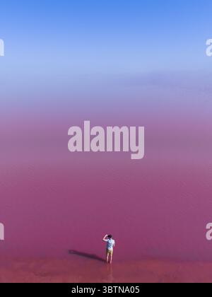 Vue aérienne d'une figure solitaire debout dans les eaux roses vibrantes de Hutt Lagoon, une scène d'un autre monde aux teintes contrastées, Australie occidentale, Australie occidentale, Australie. Banque D'Images
