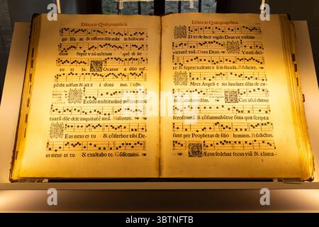Pages ouvertes d'un ancien livre liturgique montrant des chants latins et des notations musicales, illuminé par une lumière chaude au Musée Cerveny Klastor, Slovaquie Banque D'Images