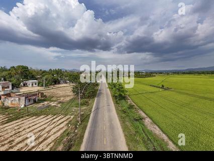Vue aérienne d'une route droite coupe à travers un paysage verdoyant, contrastant les champs cultivés avec les montagnes lointaines, Kon Tum, Kon Tum, Vietnam. Banque D'Images