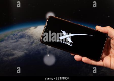 BOGOTA, COLOMBIE - 14 JUILLET 2025 Une main masculine tenant un smartphone avec sa main droite avec le logo Starlink et une planète Terre floue dans l'espace à l'arrière Banque D'Images