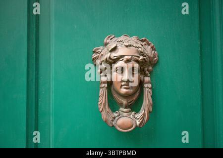 Butoir de porte en bronze vintage en forme de tête de femme avec des caractéristiques classiques, monté sur une porte en bois vert. Banque D'Images
