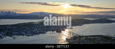 Paysage urbain de Tromsø sous le soleil de minuit, avec le pont de Tromsø traversant le fjord et des montagnes enneigées en arrière-plan, nord de la Norvège Banque D'Images
