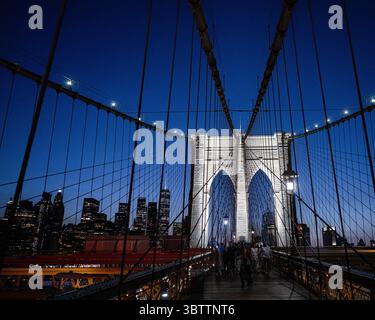 Piétons du pont de Brooklyn marchant au coucher du soleil le soir et la nuit tombent en gros plan sur les câbles de promenade et les arches en pierre dans Lower Manhattan New York City Banque D'Images