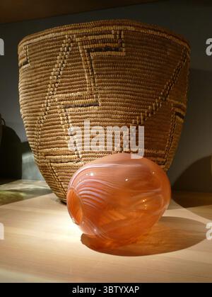 SEATTLE - APR 25, 2025 - panier tissé avec des motifs géométriques et un vase en verre orange avec des tourbillons blancs affichés sur une surface en bois clair, con Banque D'Images