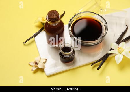 Extrait de vanille en bouteilles, gousses de vanille et fleurs sur fond jaune Banque D'Images