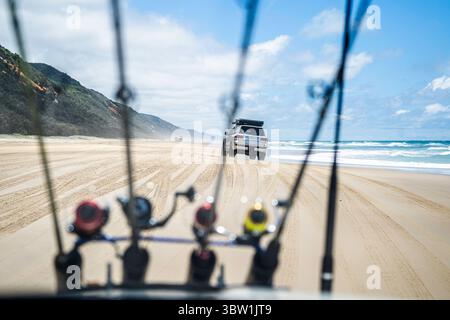Véhicules 4x4 conduisant sur une large plage de sable vue à travers des cannes à pêche montées sur le capot, Teewah Beach, parc national de Great Sandy, Queensland, Australie Banque D'Images