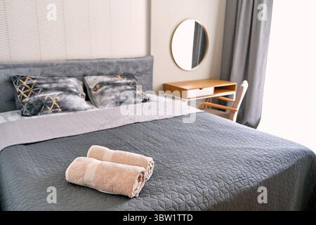 Une chambre élégante et moderne avec literie grise et oreillers décoratifs sur un lit confortable, rehaussé par un bureau en bois, une chaise et un mi rond élégant Banque D'Images