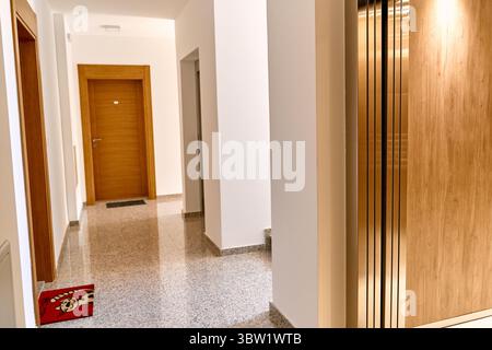 Couloir lumineux et moderne dans un immeuble résidentiel avec portes en bois, planchers de granit et un ascenseur avec des reflets métalliques, mettant en valeur a élégant Banque D'Images