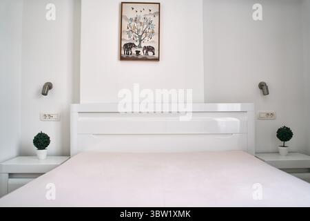 Cette chambre minimaliste dispose d''un lit blanc élégant, d''œuvres d''art murales modernes et de plantes vertes en pot. le décor reflète simplicité et tranquillité. Banque D'Images