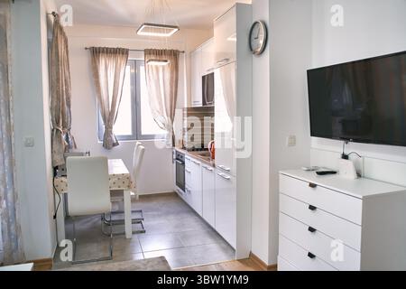 Une cuisine-salle à manger moderne et lumineuse avec des armoires blanches minimalistes, un mobilier élégant et un éclairage élégant améliore la fonctionnalité et le style. Banque D'Images