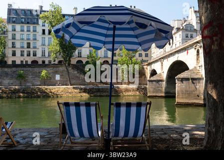 Chaises de plage rayées bleues et blanches et parasol sur la rive de la Seine pour Paris plage, une plage artificielle le long de la Seine Banque D'Images