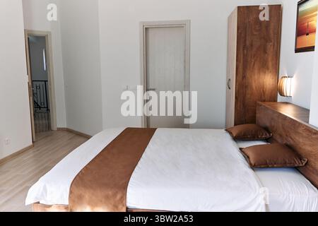 Une chambre minimaliste avec un lit confortable avec un cadre en bois, des murs blancs et un décor élégant, créant une ambiance sereine et élégante parfaite f Banque D'Images
