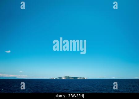 Une petite île entourée d'une vaste étendue d'océan bleu sous un ciel clair. Banque D'Images