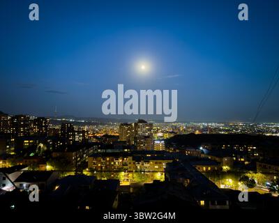 La ville est illuminée la nuit avec une pleine lune brillante dans le ciel. La lune est positionnée au milieu du ciel, projetant une douce lueur sur th Banque D'Images