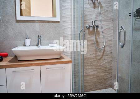 Salle de bains élégante dispose d'un lavabo moderne et cabine de douche en verre, complétée par un comptoir en bois naturel et des luminaires élégants, offrant un Banque D'Images