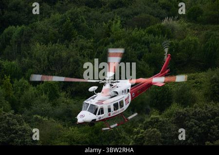 Hélicoptère de sauvetage rouge et blanc volant au-dessus d'une forêt verdoyante, fournissant des services médicaux d'urgence et des opérations de recherche et de sauvetage Banque D'Images