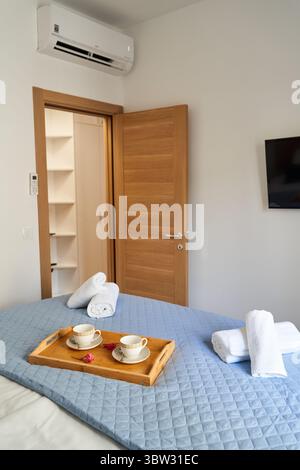 Une chambre moderne avec une porte en bois, air conditionné, et un lit confortable avec du thé sur un plateau, créant une atmosphère accueillante et sereine. Banque D'Images