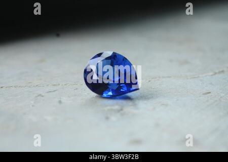 Une pierre précieuse de saphir bleu royal en forme de poire taillée sur une surface de pierre blanche sous la lumière naturelle. Banque D'Images