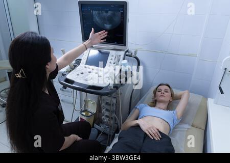 Professionnel de la santé expliquant les résultats de l'échographie au patient pendant l'examen dans un cadre clinique, avec équipement et atmosphère détendue Banque D'Images