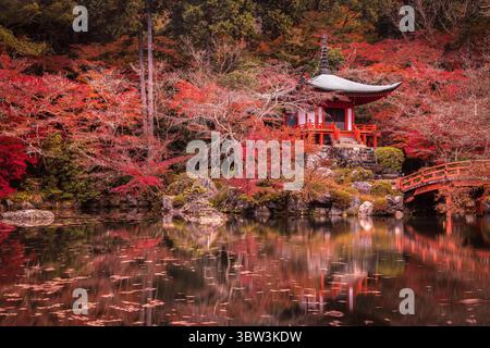 Vue d'une pagode rouge vibrante nichée au milieu d'un feuillage automnal ardent reflété dans les eaux sereines d'un étang, Kyoto, Kyoto, Japon. Banque D'Images