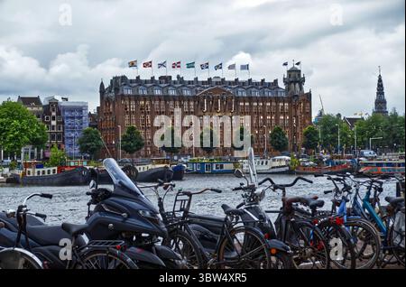 Vélos appuyés contre des bâtiments historiques au bord de la rivière, capturant le paysage urbain emblématique d'amsterdam et la culture cycliste le long de la rivière amstel Banque D'Images