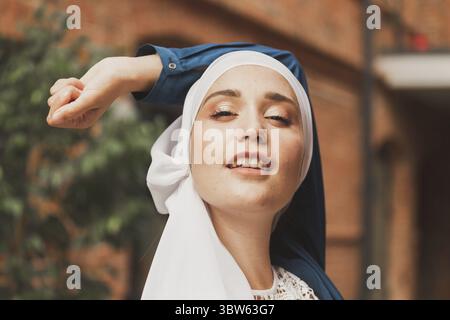 Portrait d'une jeune femme musulmane portant un foulard hijab en ville tout en regardant l'appareil photo. Gros plan de femme gaie couverte d'un foulard souriant Banque D'Images