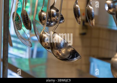 Un ensemble de cuillères et de cuillères de cuisine en métal est suspendu à un rail dans une cuisine professionnelle Banque D'Images