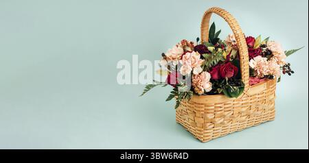 C'est un bouquet de fleurs délicates dans un panier en osier sur fond bleu de couleur pastel. Bannière de félicitations avec espace pour la copie. Somme Banque D'Images