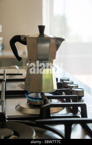 Un pot de moka italien classique préparant un expresso frais sur une cuisinière à gaz, avec une flamme bleue visible chauffant la cafetière traditionnelle dans un kitc maison moderne Banque D'Images
