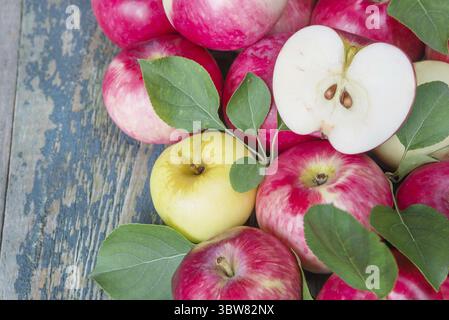 Beaucoup de pommes rouges avec des feuilles vertes sur la vieille table en bois Banque D'Images