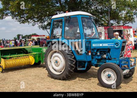 Un tracteur Ford 4600 bleu, tirant un John Deere Bailer vert et jaune lors d'un salon de campagne par une journée ensoleillée. Banque D'Images