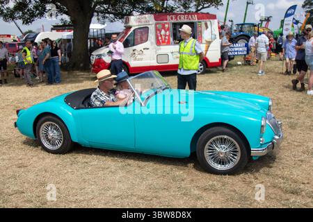 Une MG des années 1950 Une voiture à moteur en bleu/aigue-marine conduite par un homme portant un chapeau de paille lors d'un défilé de campagne/rallye de voitures anciennes en Angleterre. Banque D'Images