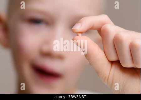 L'enfant tient la dent de bébé tombée dans ses mains, la regardant, en gros plan. Dentisterie infantile, soin des dents infantiles. Vertical. Banque D'Images