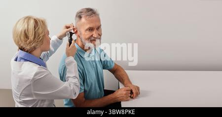 Homme âgé alors que test d'oreille avec audiologiste avec otoscope au cabinet médical, gros plan. Diagnostic de déficience auditive, bilan de santé, otoscopie Banque D'Images