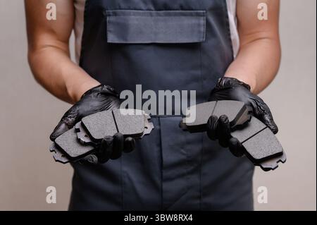 Mécanicien automatique en combinaison tenant quatre plaquettes de frein dans les mains, gros plan, se préparant à les remplacer. Concept d'entretien, facilité d'entretien du système de frein de voiture Banque D'Images