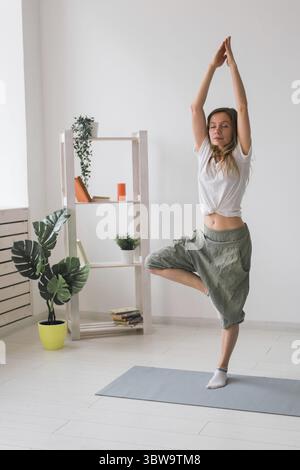 Femme pratique le yoga effectue. Posez sur mat à l'intérieur de la chambre confortable avec des plantes et de la verdure. Concept de mode de vie sain Banque D'Images