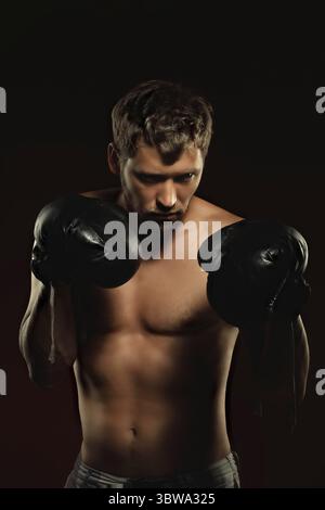Voici un portrait spectaculaire d'un boxeur en vieux gants de boxe sur fond sombre. Un combattant athlétique des arts martiaux mixtes se tient en position de combat. Banque D'Images