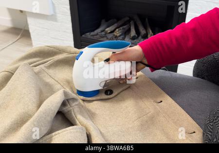 Femme utilisant un rasoir anti-boulochage à la maison. Dispositif pour le rasage de vêtements. Rasoir anti-peluche. Chandail portatif électrique pour défuzzer pilules. Mode lente Banque D'Images