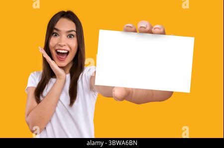 Portrait de la jeune femme caucasienne excitée tenant une carte vierge de papier blanc avec maquette pour vos informations d'affaires Banque D'Images